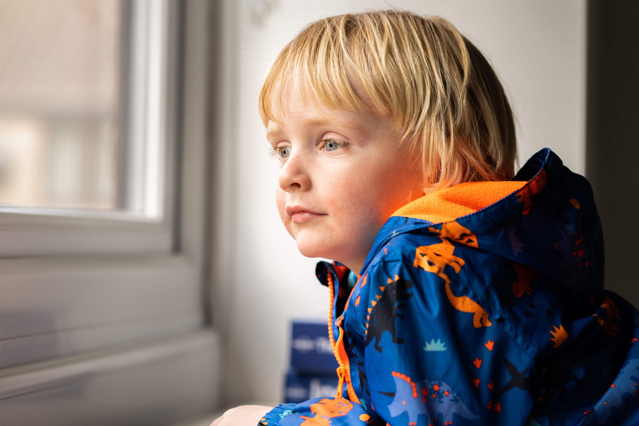 A child looking thoughtfully through a bright window