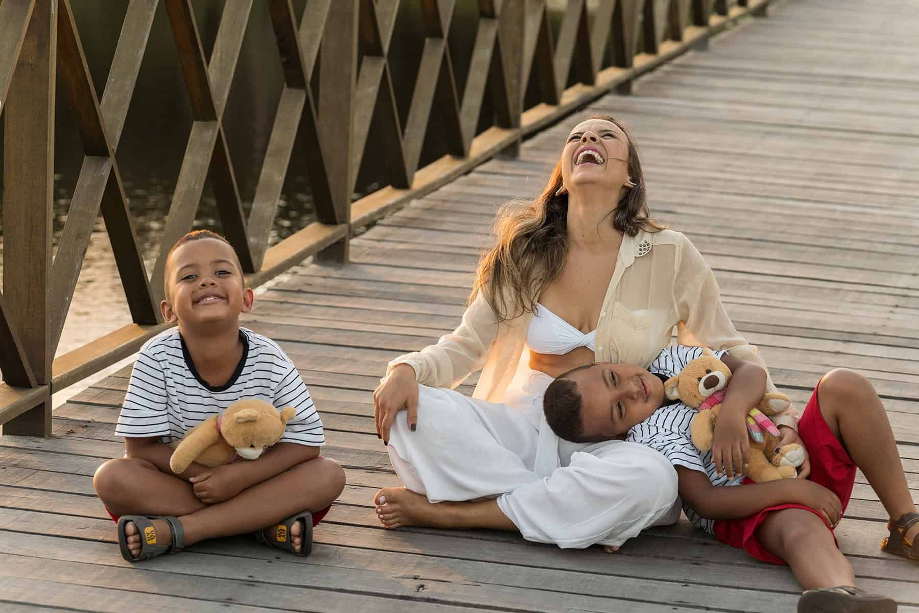A mother relaxing with her two children and their teddy bears on a wooden walkway