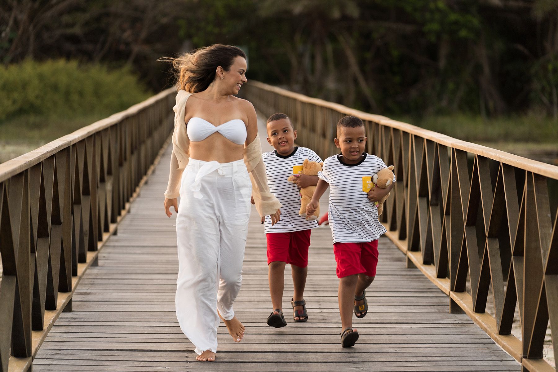 A mother walking with her two children along a wooden bridge at sunset