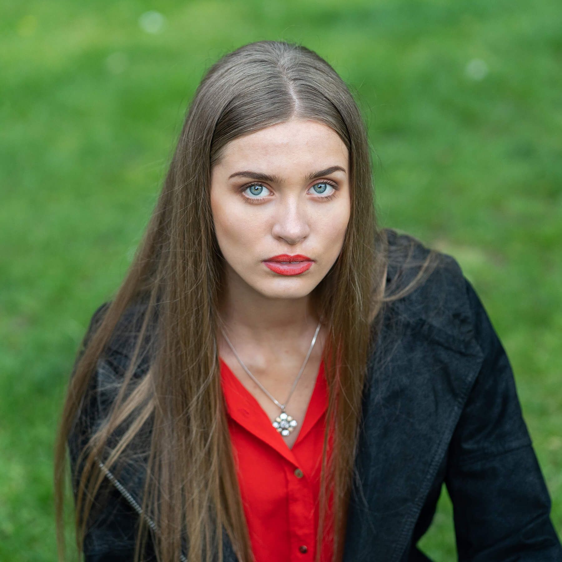 An editorial portrait of a woman in red against a green landscape