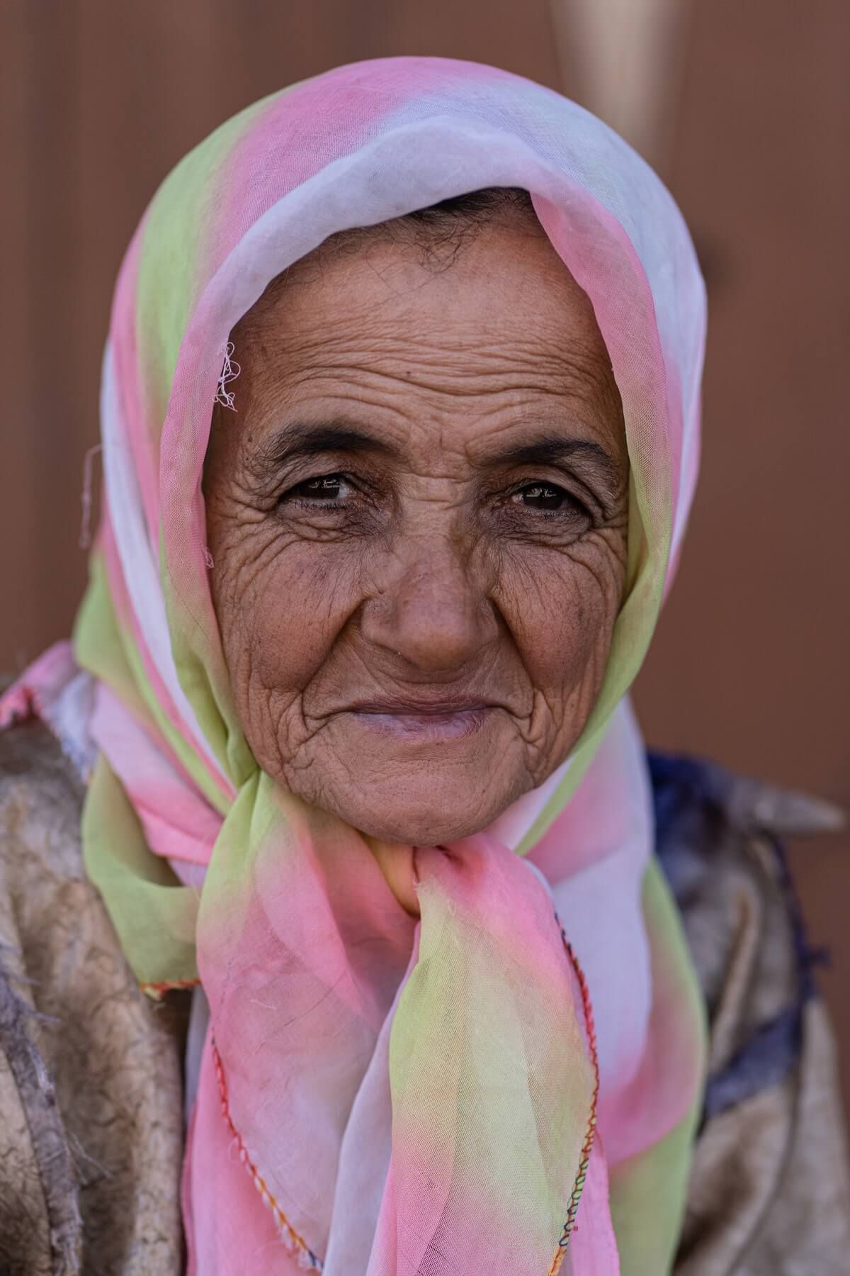 A close portrait of an older woman wearing a softly coloured headscarf